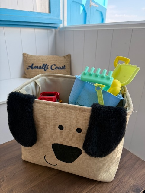 A dog-shaped basket filled with buckets, spades, rakes and other beach toys.