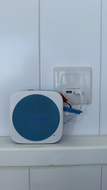 A blue Bluetooth speaker on a shelf next to a plug socket with USB charging points.